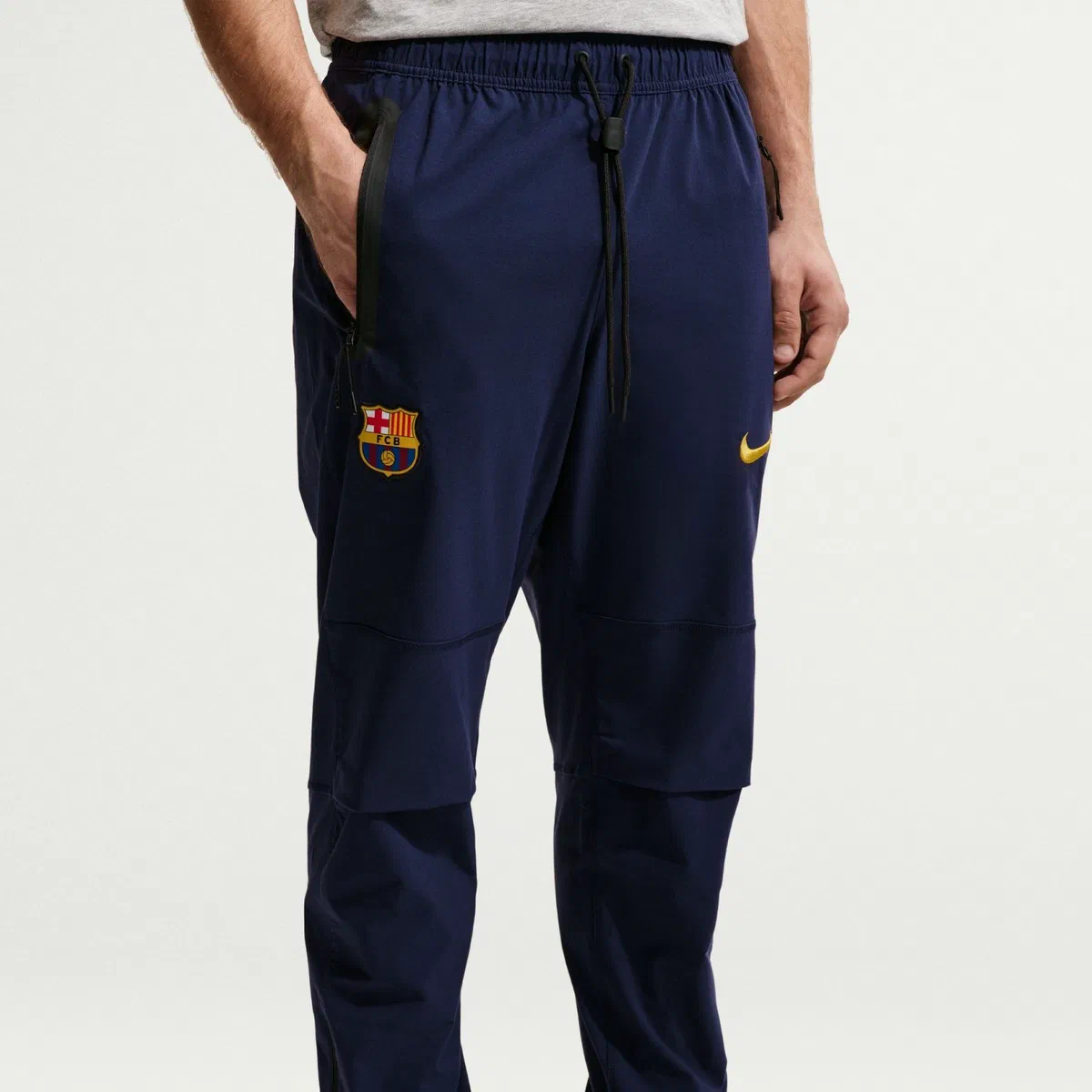 Pantalon Tech Woven FC Barcelone bleu foncé porté, poche zippée et écusson sur la cuisse