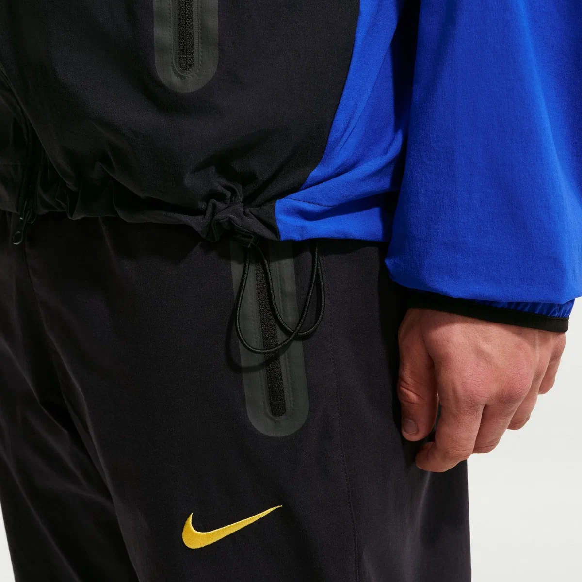 Bas de la veste Tech Woven Chelsea, cordon de serrage, swoosh doré et manche bleu roi